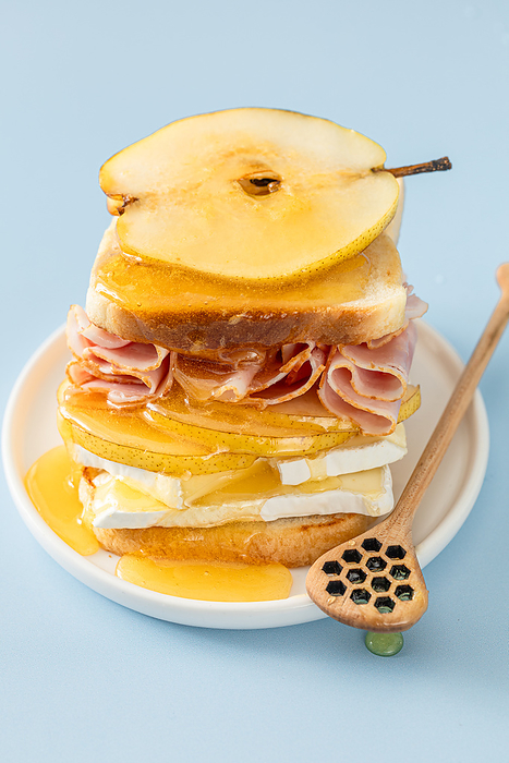 sandwich with layers of ham, brie, and pear with golden honey, by Cavan Images / Galigrafiya