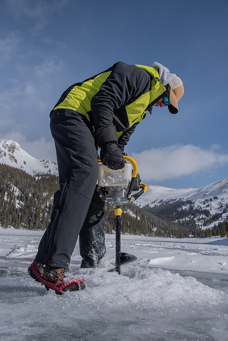 Man drills an ice fishing hole in Colorado mountains, by Cavan Images / Doskophoto