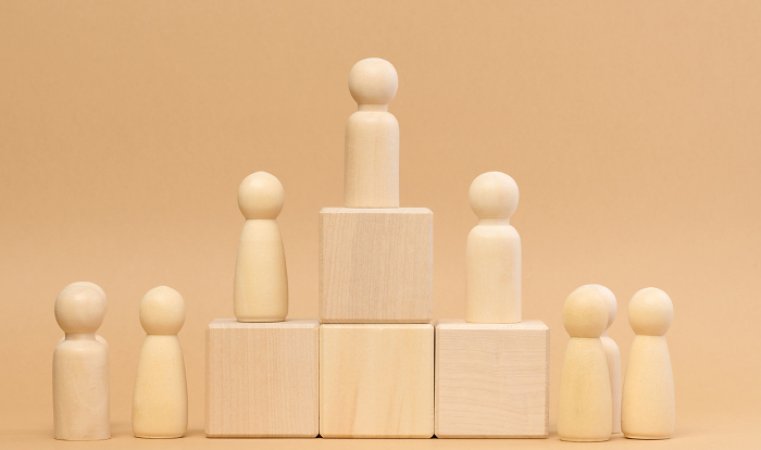 Wooden figures of men stand on a pedestal. The concept of rivalry in sports, business and life. Achieving success and leadership Wooden figures of men stand on a pedestal. The concept of rivalry in sports, business and life. Achieving success and leadership