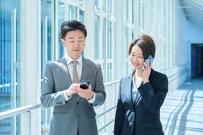 Japanese man and woman in suits operating smartphones (People)