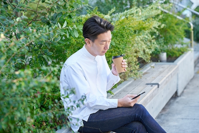 Japanese man operating smartphone while drinking coffee (People)