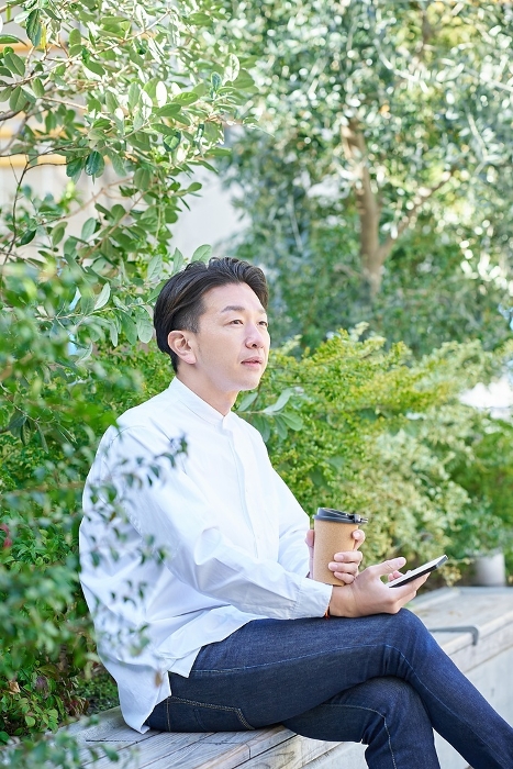 Japanese man operating smartphone while drinking coffee (People)