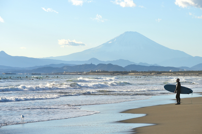 Surfer standing on Tsujido Beach with a view of Mt.
