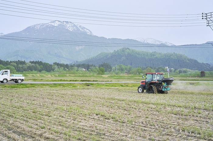 Photographed in 2024 Rice cultivation in Minamiuonuma   Fertilizer application April 2024 Minamiuonuma City, Niigata Prefecture Spraying fertilizer containing minerals and other nutrients before raising rice paddies. The snow covered mountain in the background is Mt.