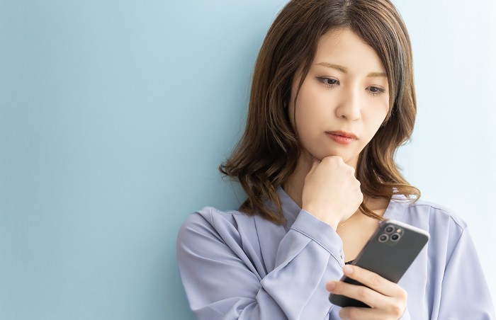 Japanese woman looking at her smartphone and thinking seriously (People)