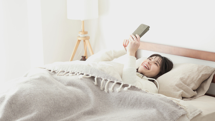 Asian woman looking at her phone when she wakes up from sleep （Japanese / People)