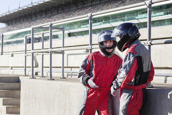   Two racers in helmets having a conversation at the race track.