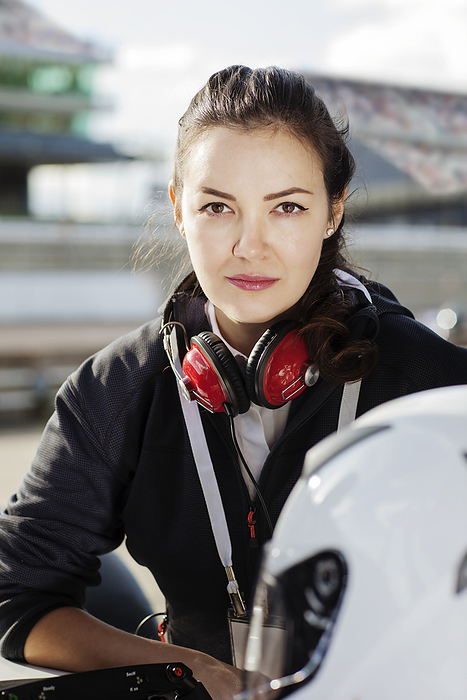 Young woman with headphones around neck standing confidently in urban setting.