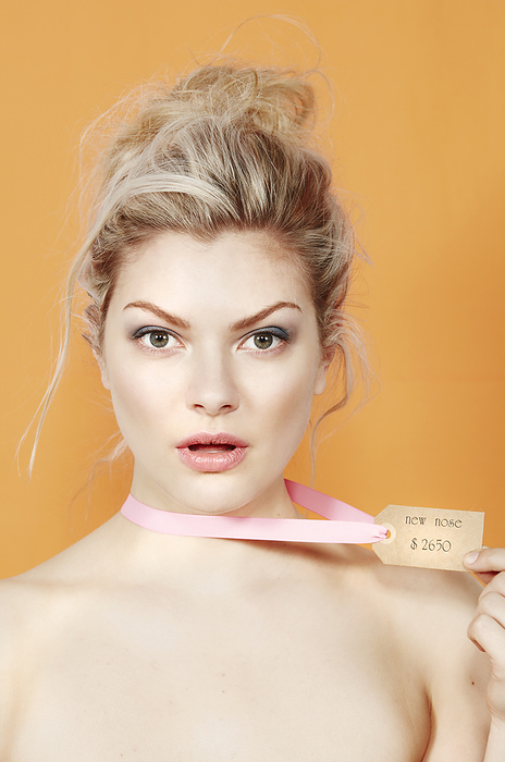 Young woman holding a price tag with a thoughtful expression against an orange background