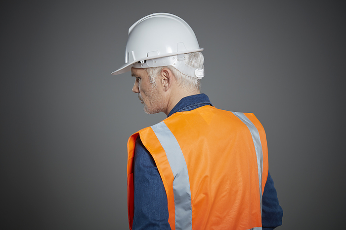Mature construction worker in reflective vest and helmet looking to the side.