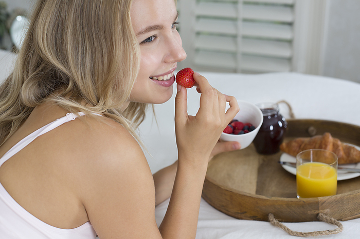 Young woman eating breakfast in bed.