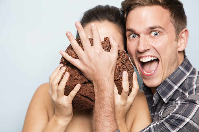 Young man pushing chocolate cake into young woman's face