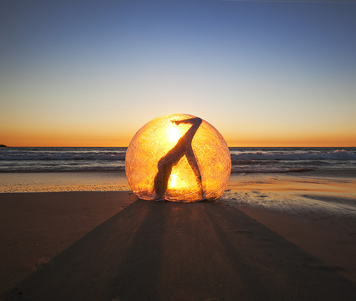Silhouette of a person inside a glowing orb on the beach at sunset