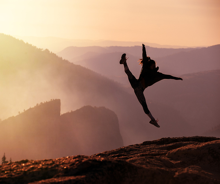 Silhouette of a person joyfully leaping at the edge of a mountain during sunset