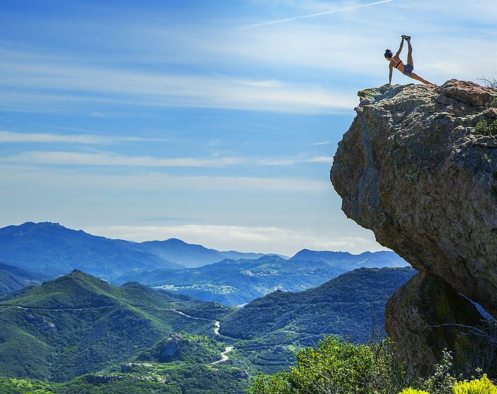 Young woman doing yoga on mountain rock