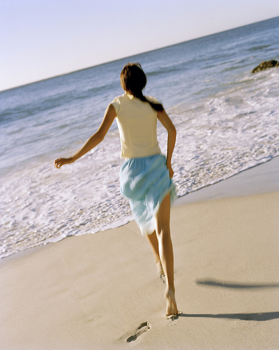 Young woman wearing blue skirt running on beach