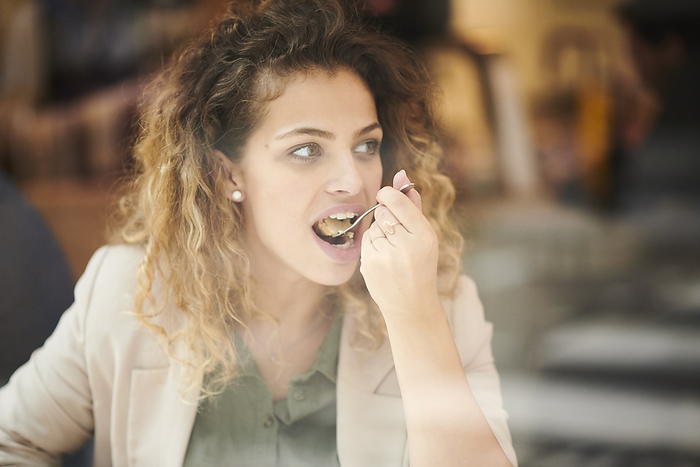 Young woman eating cake behind cafe window