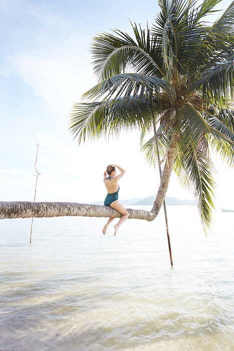 Young woman sitting on palm tree at beach