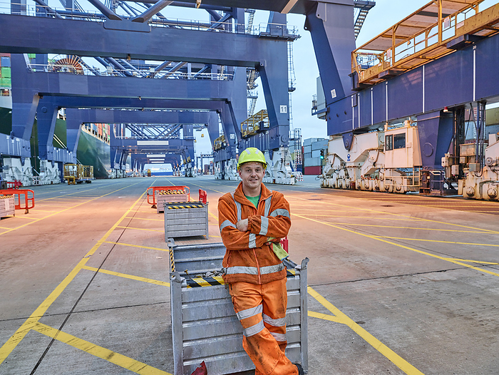 Portrait of dock worker waiting for cargo to be loaded from crane