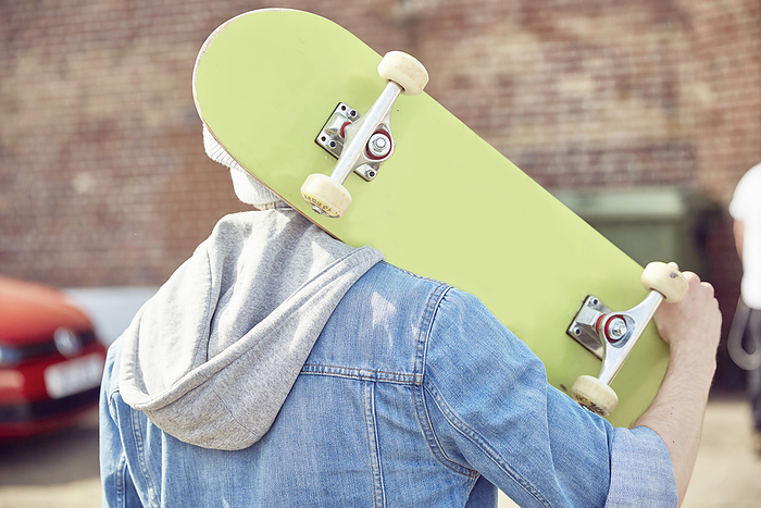 Rear view of teenage boy carrying skateboard