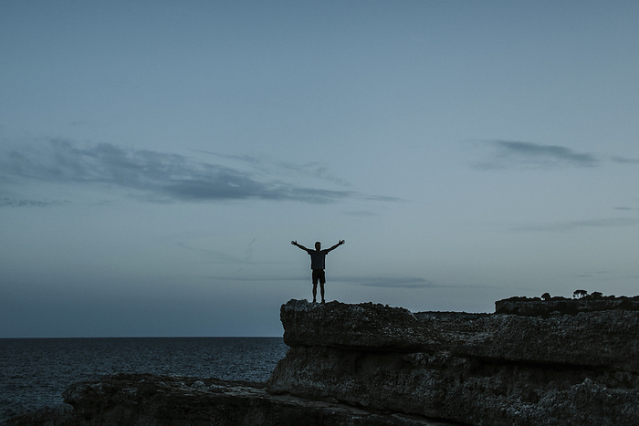 Silhouette of a young man with arms outstretched on rocks at Calo des Moro in Mallorca