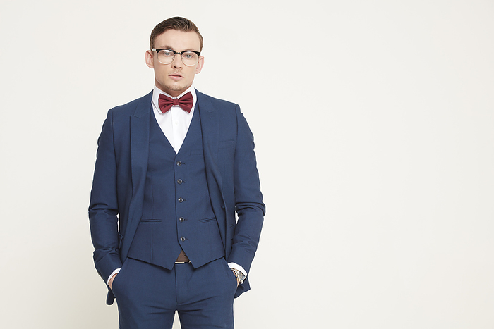 Young man in stylish blue suit and red bowtie posing confidently against a neutral background