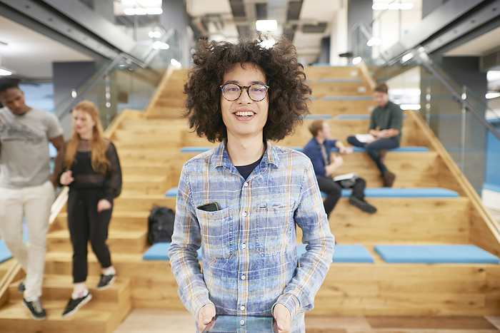 Smiling person with curly hair standing in a modern office stairway with colleagues in the background.