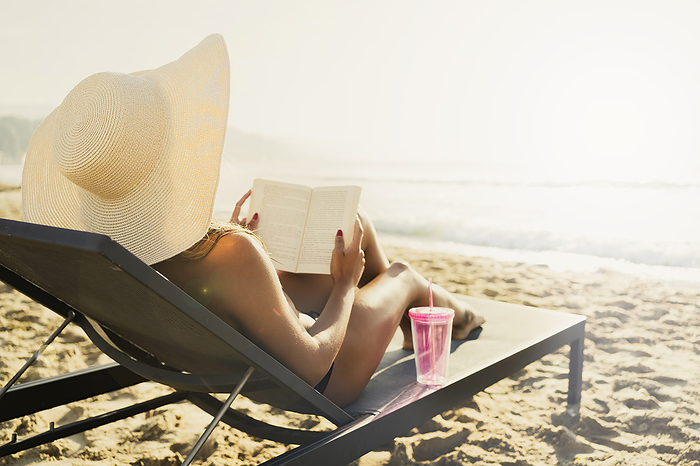 Woman reclining on deck chair and reading book at beach