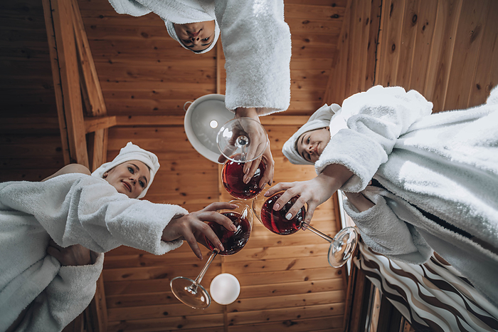 Friends wearing bathrobes and toasting wine at sauna