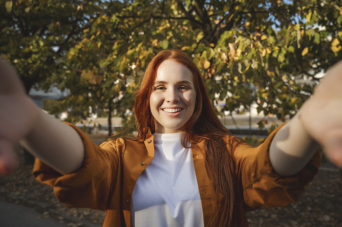 Smiling woman taking selfie near tree in autumn