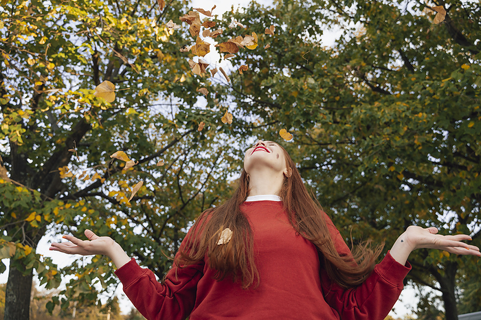 Redhead woman playing with autumn leaves under tree at park