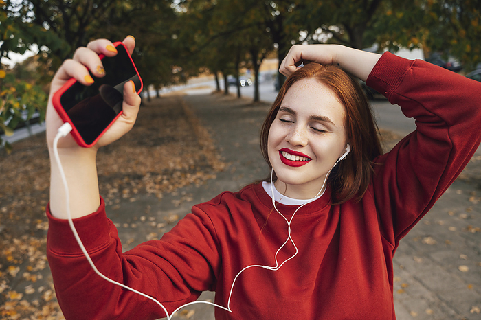 Happy woman listening to music with eyes closed in autumn