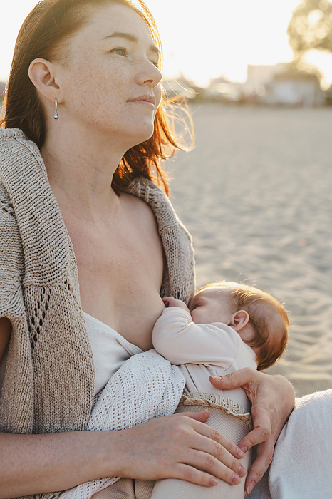Woman breastfeeding baby girl at beach