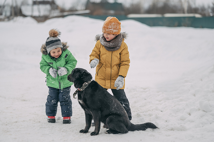 Happy children wearing warm clothes and playing with dog in snow
