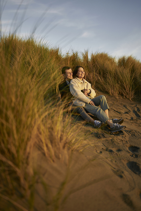 Smiling young couple sitting in dune at beach