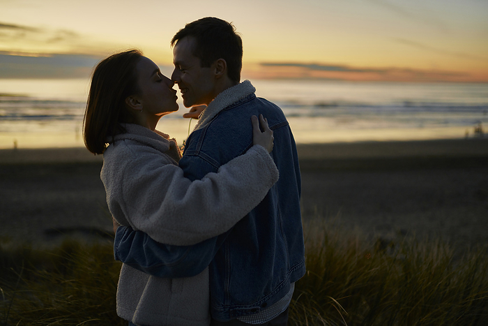 Affectionate girlfriend and boyfriend embracing on beach at sunset