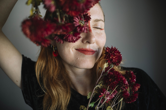 Smiling woman with eyes closed holding flowers against gray background