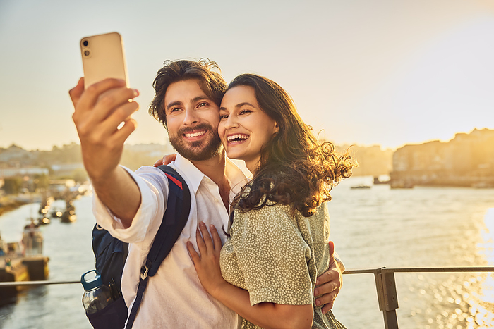Happy couple taking selfie through smart phone in front of Douro river at sunset