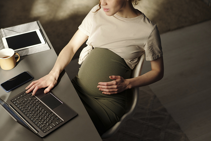 Pregnant freelancer using laptop at desk in home office