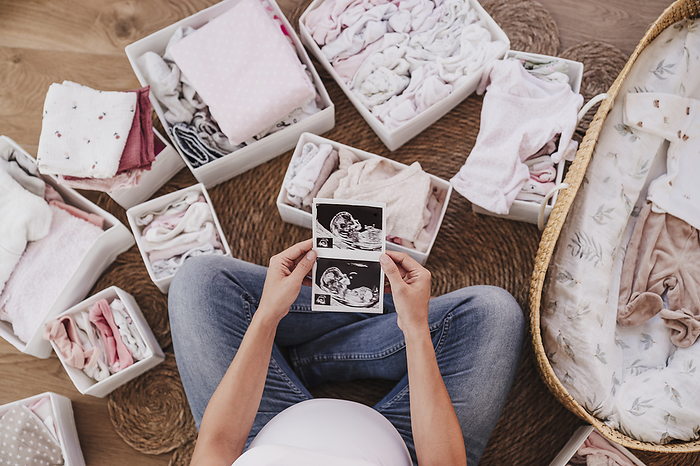 Pregnant woman sitting on floor and holding ultrasound photographs at home