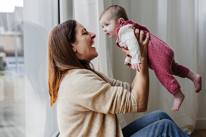 Happy mother holding baby daughter in front of window