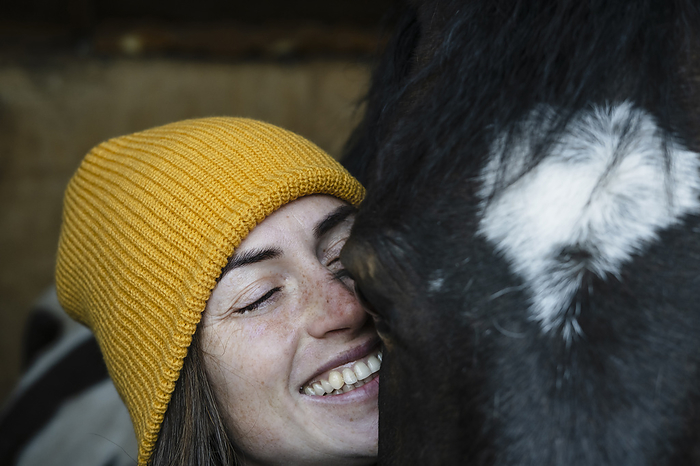 Happy woman with eyes closed near piebald horse in stable