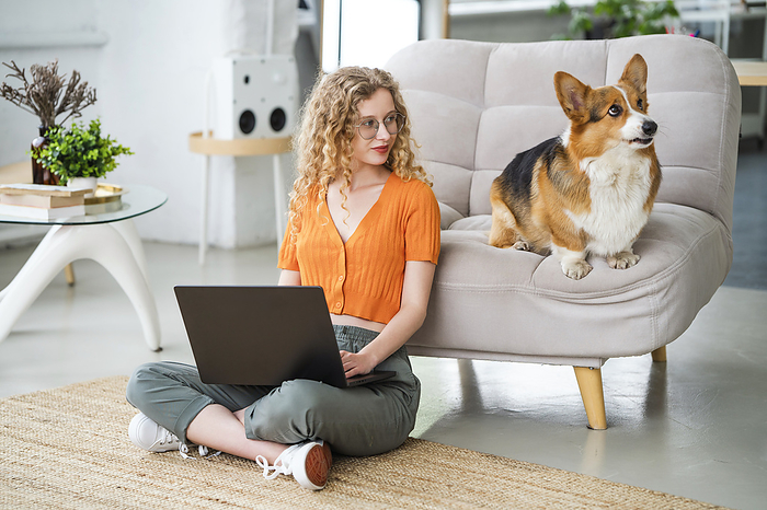 Freelancer sitting with laptop near dog at home office