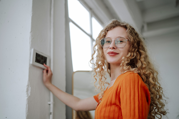 Smiling woman near thermostat on wall at home