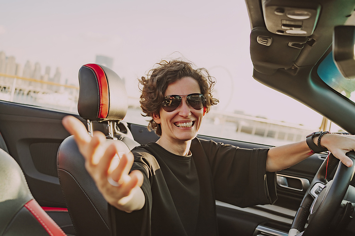 Happy woman wearing sunglasses gesturing in convertible car on sunny day