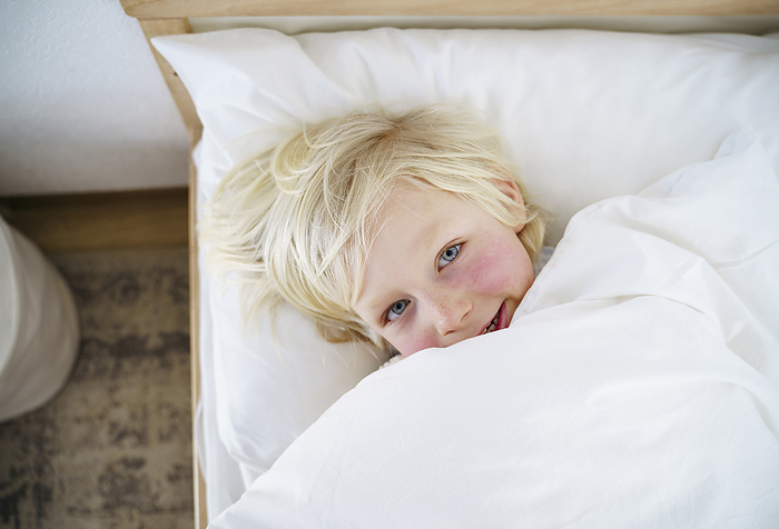 Smiling blond boy lying down on bed at home