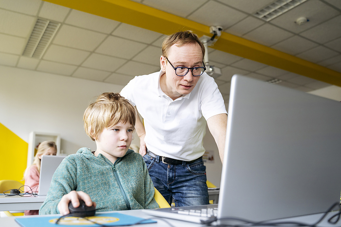 Professor assisting boy with coding in laptop at desk