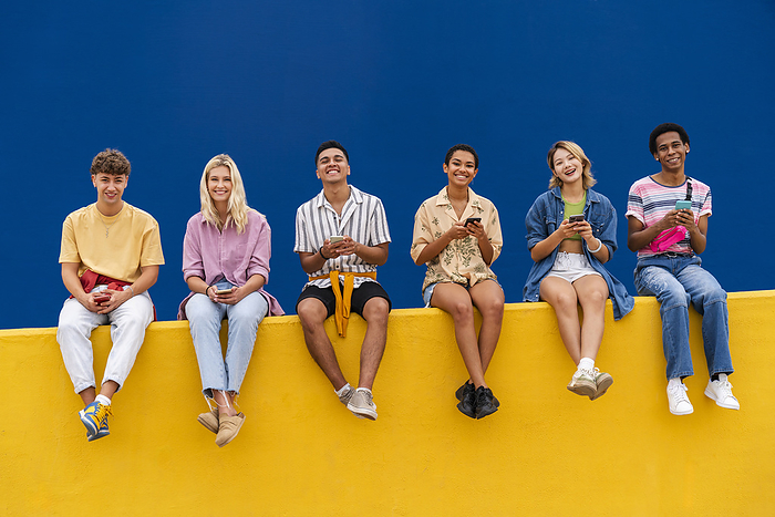 Happy friends with colorful clothing sitting on yellow using their smartphones
