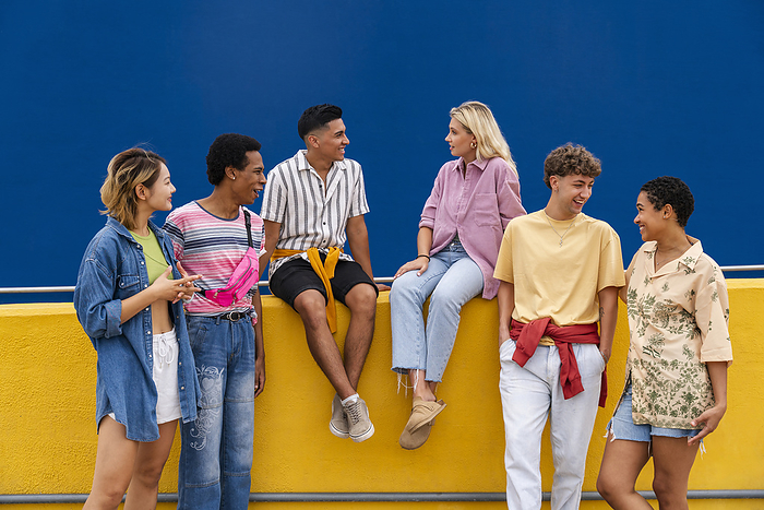 Group of friends friends with colorful clothing sitting on yellow wall chatting together