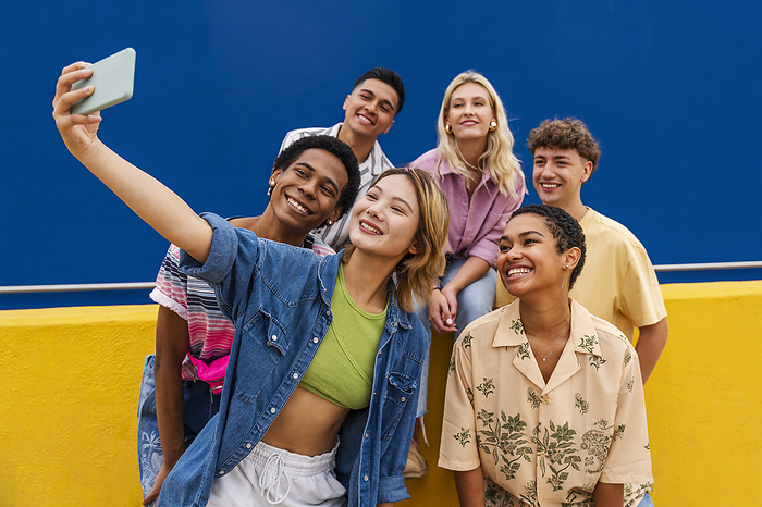 Group of friends friends with colorful clothing sitting on yellow wall taking group photo